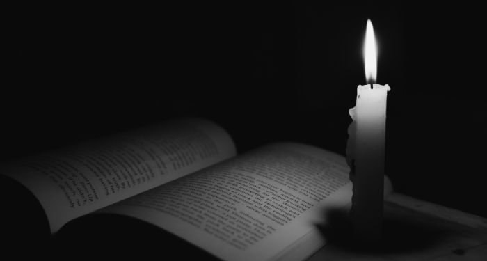 a black and white image of an open book next to a lit candle