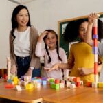a teacher supervising four elementary school children playing with building blocks